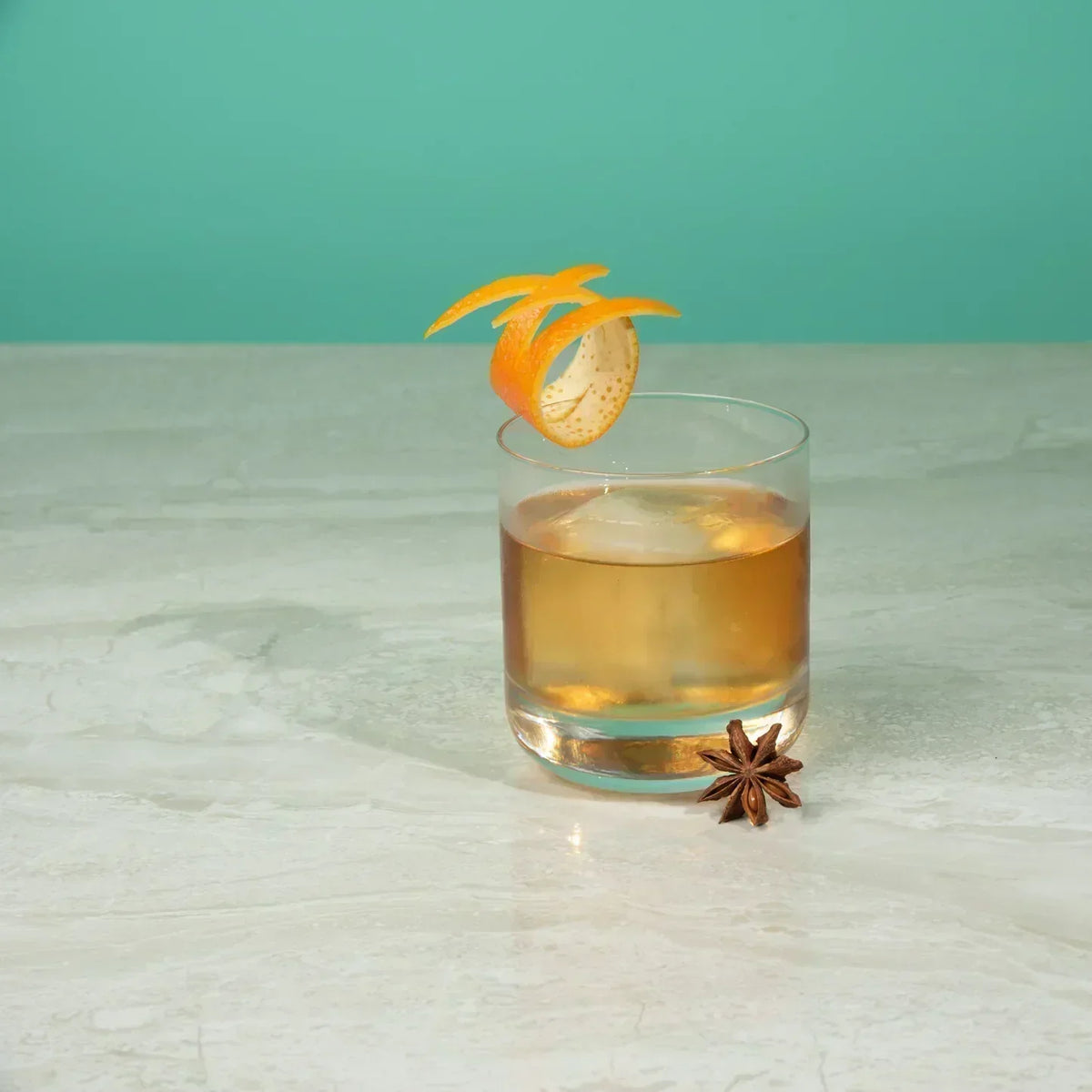 Alcoholvrije spirit in tumblerglas met sinaasappelschil en steranijs op marmeren tafel | World of NIX
