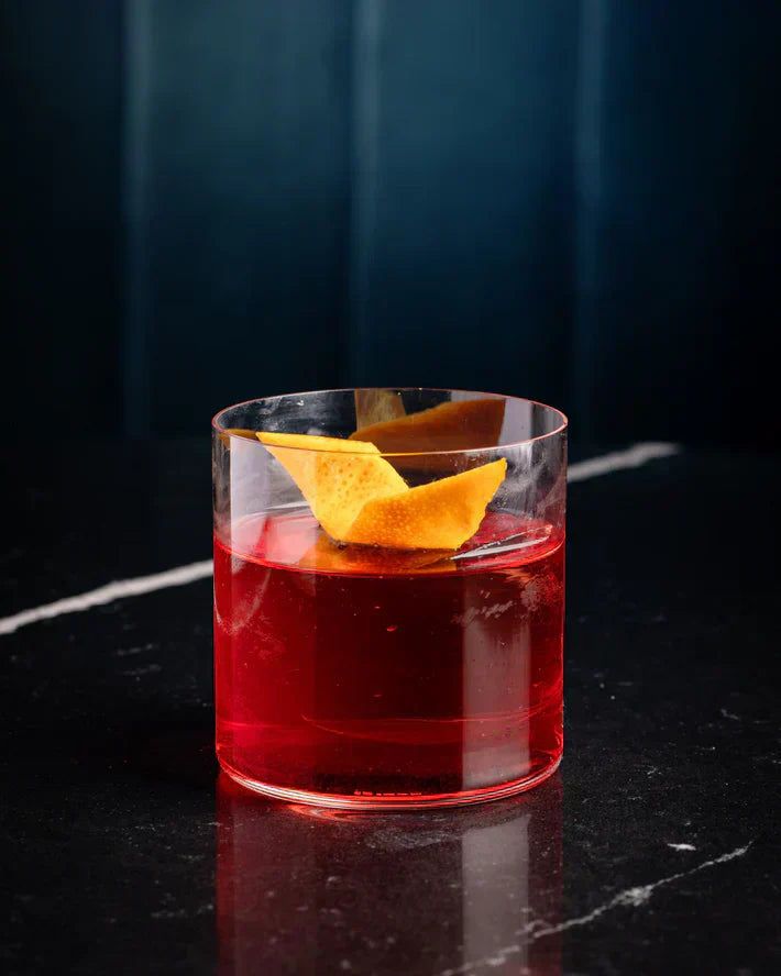 Glas rode alcoholvrije cocktail met sinaasappelschil op zwart marmer | World of NIX