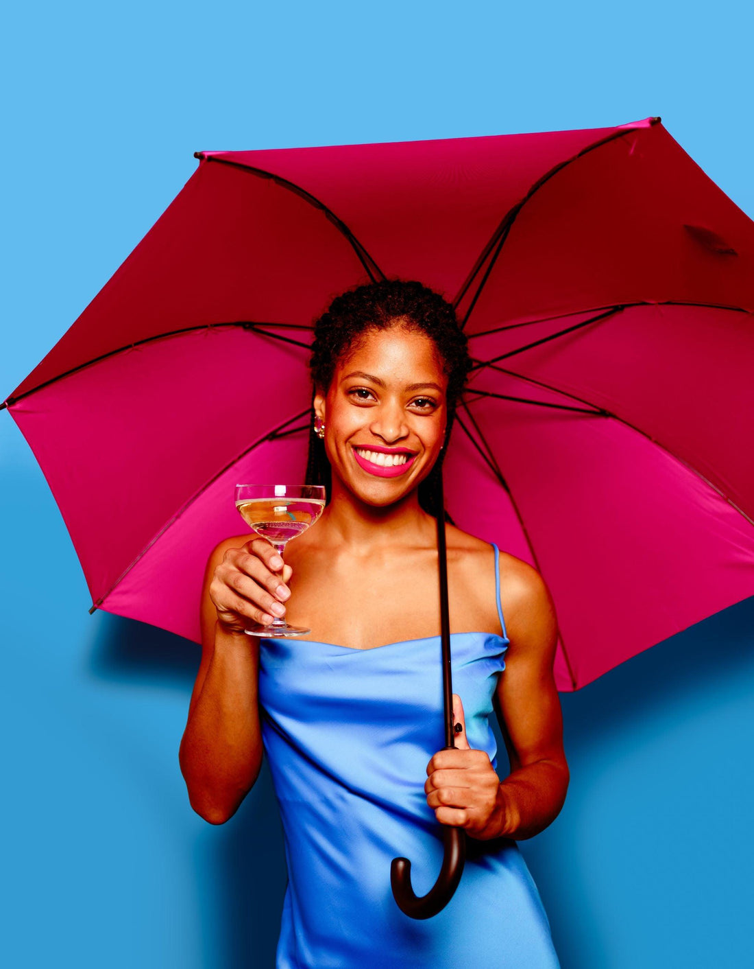 Vrouw in blauwe jurk met glas alcoholvrije wijn en roze paraplu voor blauwe achtergrond | World of NIX