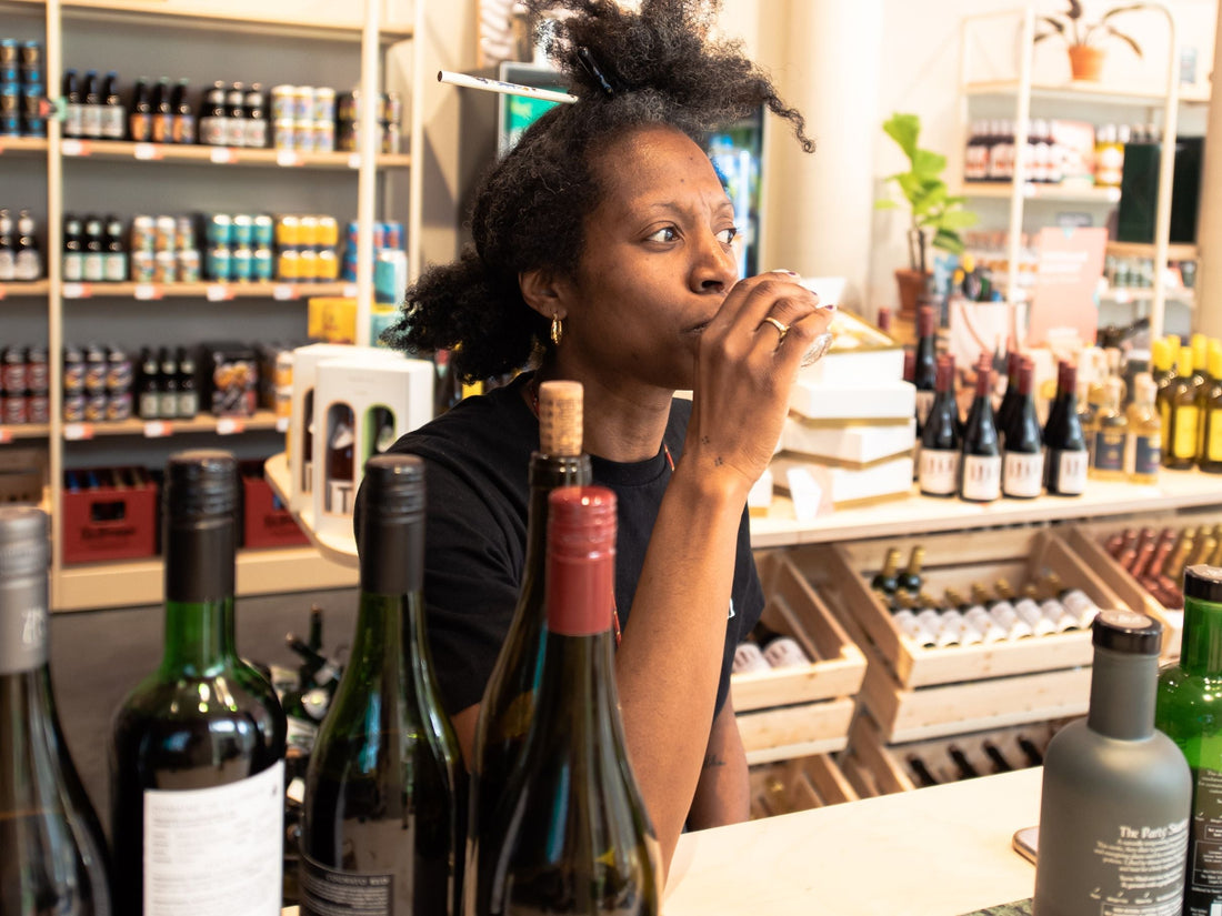 Vrouw proeft drank achter toonbank met flessen in alcoholvrije winkel | World of NIX