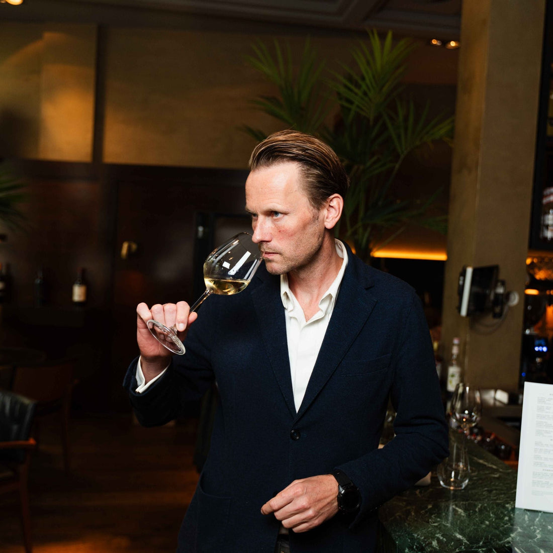 Man in een restaurant ruikt aan een glas witte wijn, stijlvolle sfeer | World of NIX