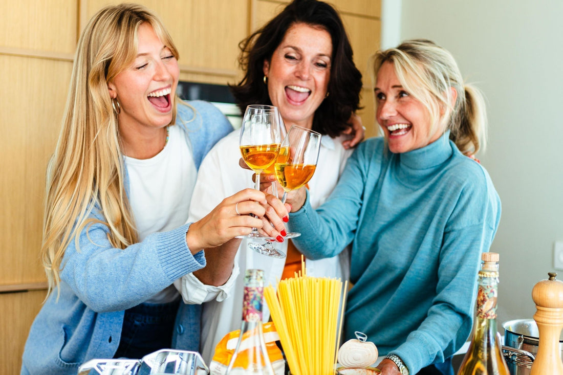 Drie lachende vrouwen proosten met alcoholvrije wijn in moderne keuken | World of NIX