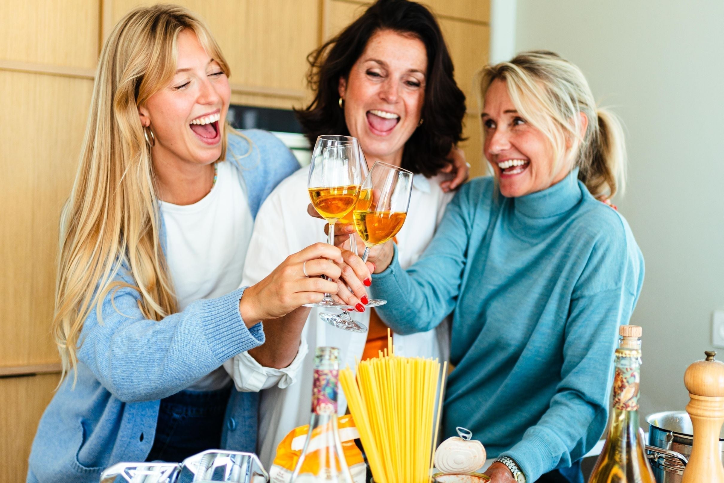 Drie lachende vrouwen proosten met alcoholvrije wijn in moderne keuken | World of NIX