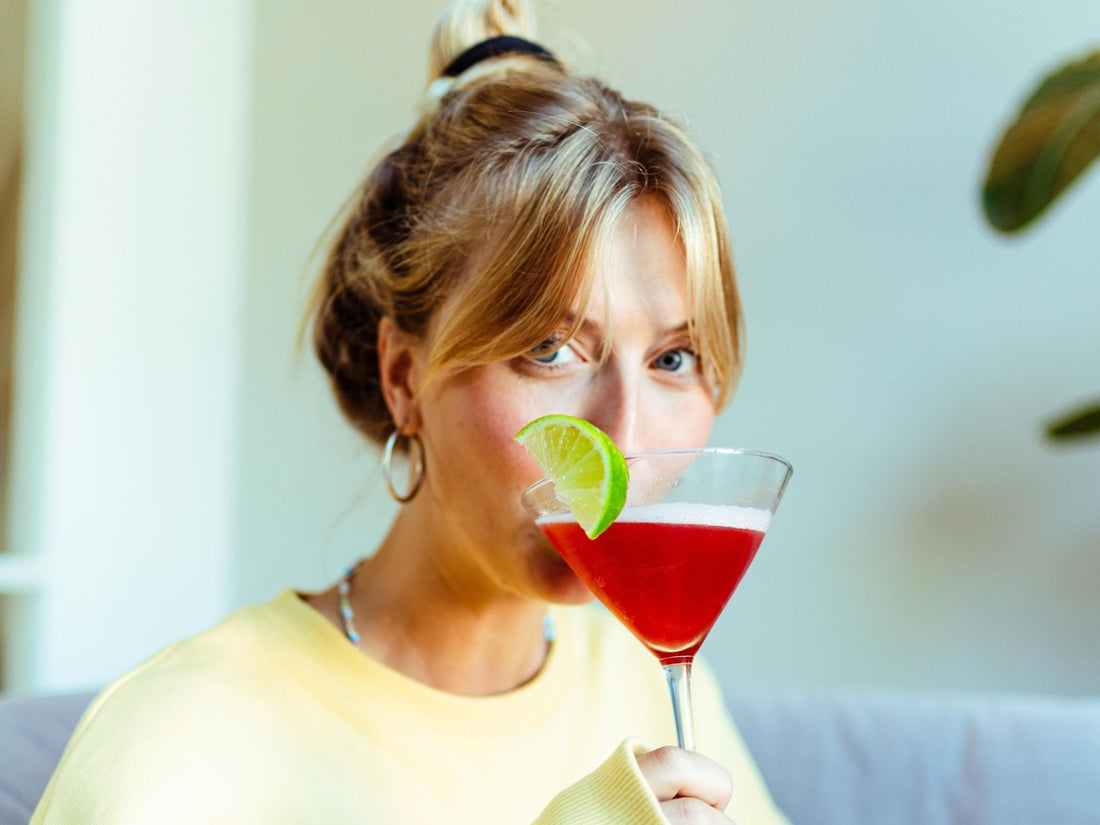 Vrouw drinkt alcoholvrije rode cocktail met limoen in martiniglas op bank | World of NIX
