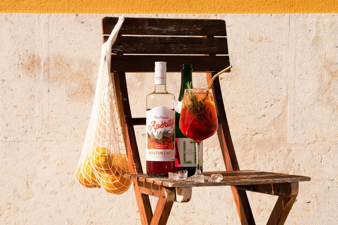 Fles alcoholvrije aperitief, cocktailglas en sinaasappels op houten stoel buiten | World of NIX