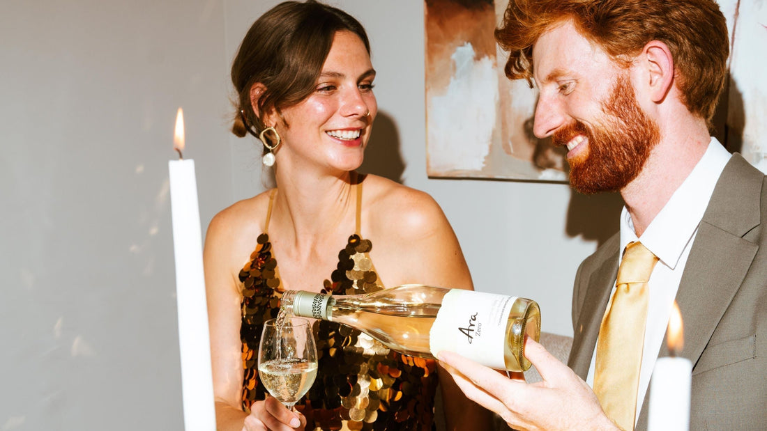 Man schenkt alcoholvrije witte wijn in voor een lachende vrouw tijdens dinerfeest | World of NIX
