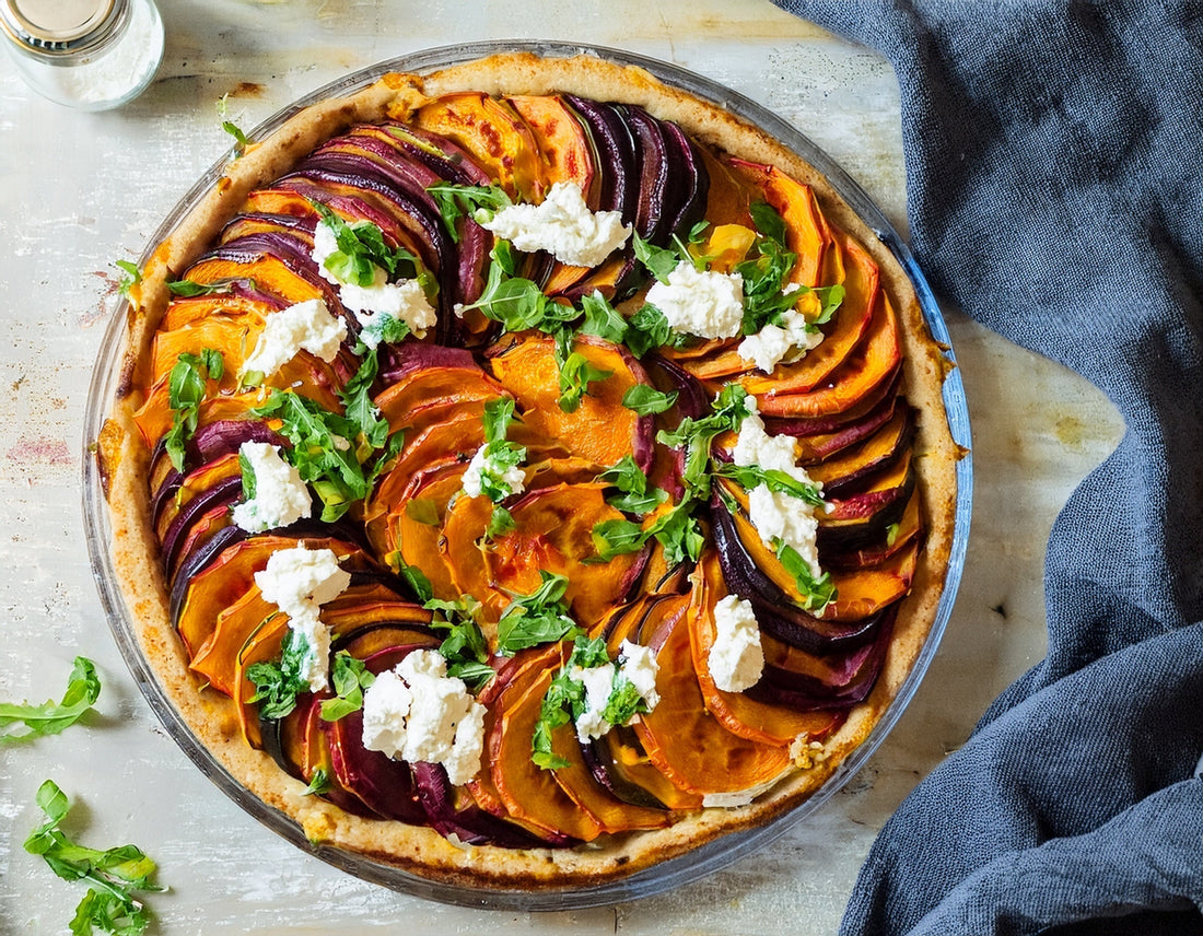 Plaattaart met zoete aardappel, biet, geitenkaas en rucola op een lichte tafel | World of NIX