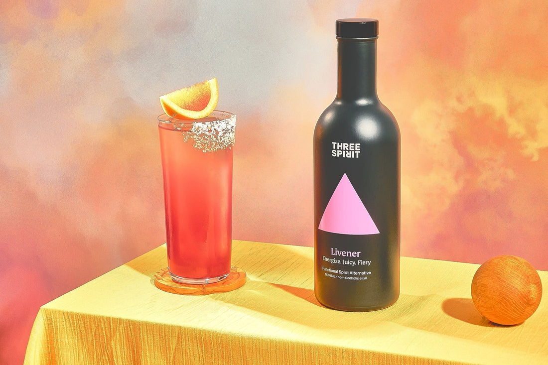 Glas alcoholvrije Paloma cocktail met sinaasappel en Three Spirit Livener fles op gele tafel | World of NIX