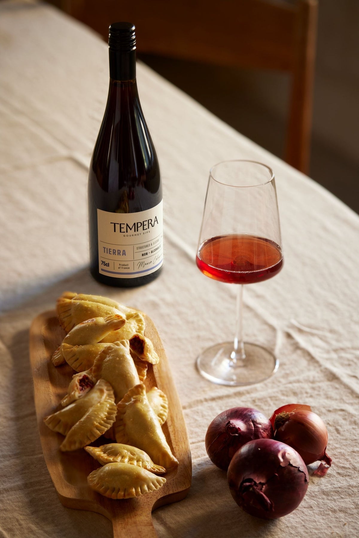 Fles Tempera Tierra alcoholvrije wijn met glas, empanadas en rode uien op tafel | World of NIX