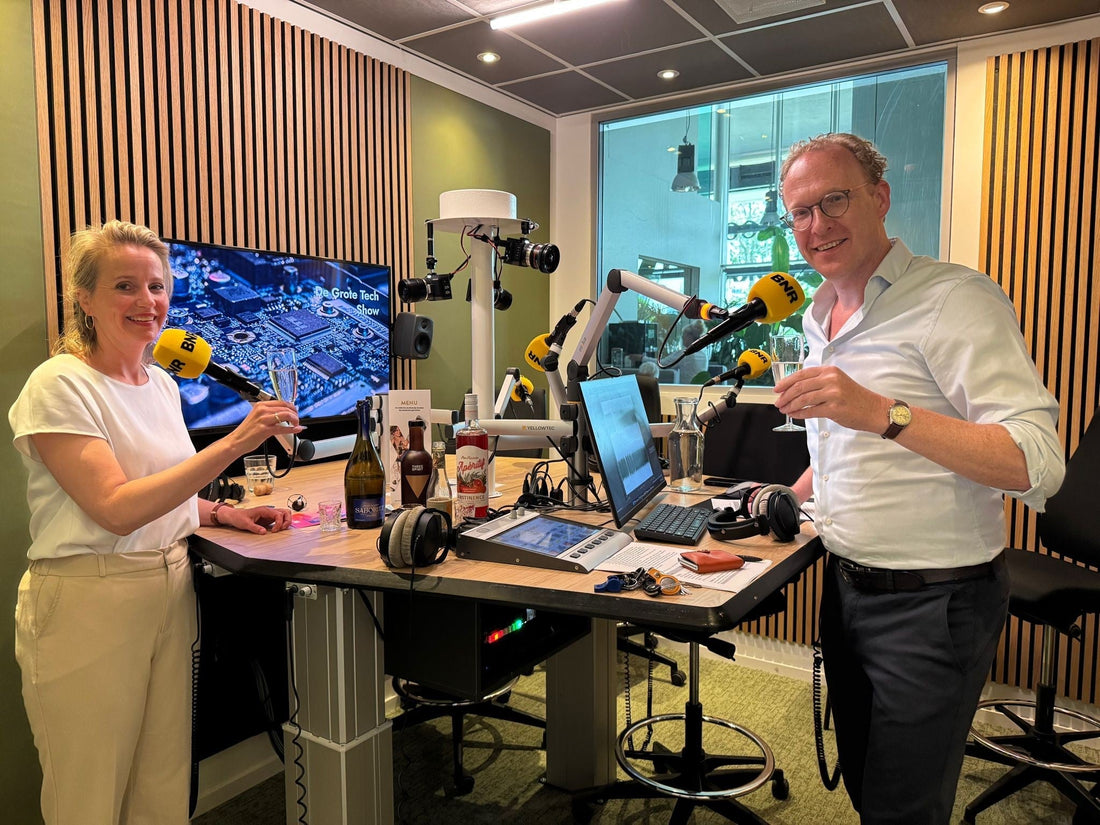 Twee personen in radiostudio proosten met alcoholvrije drank, flessen op tafel, BNR microfoons | World of NIX