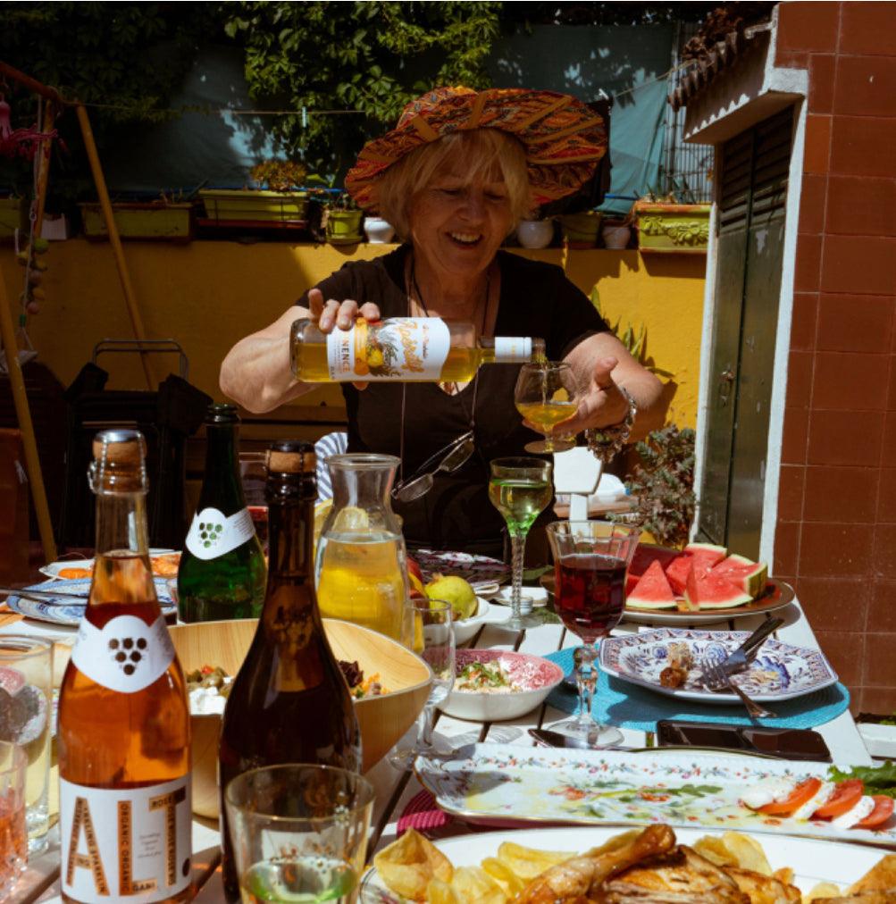 Vrouw schenkt alcoholvrije wijn aan zomerse eettafel met mocktails, watermeloen en salades | World of NIX