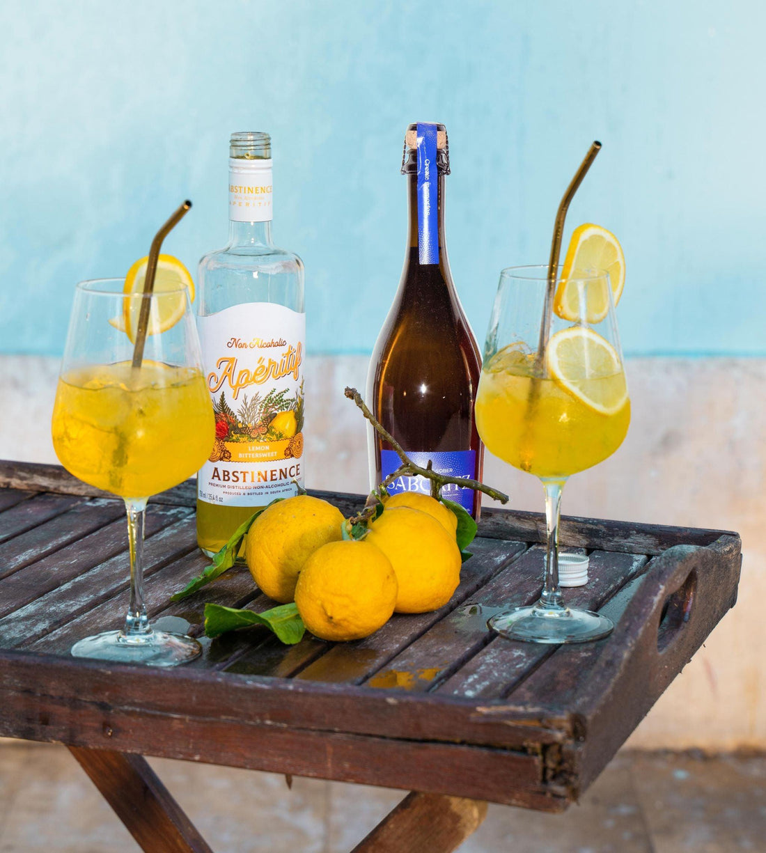 Twee alcoholvrije spritz cocktails met citroen, fles Abstinence en Sabo sprankelende drank op houten tafel | World of NIX