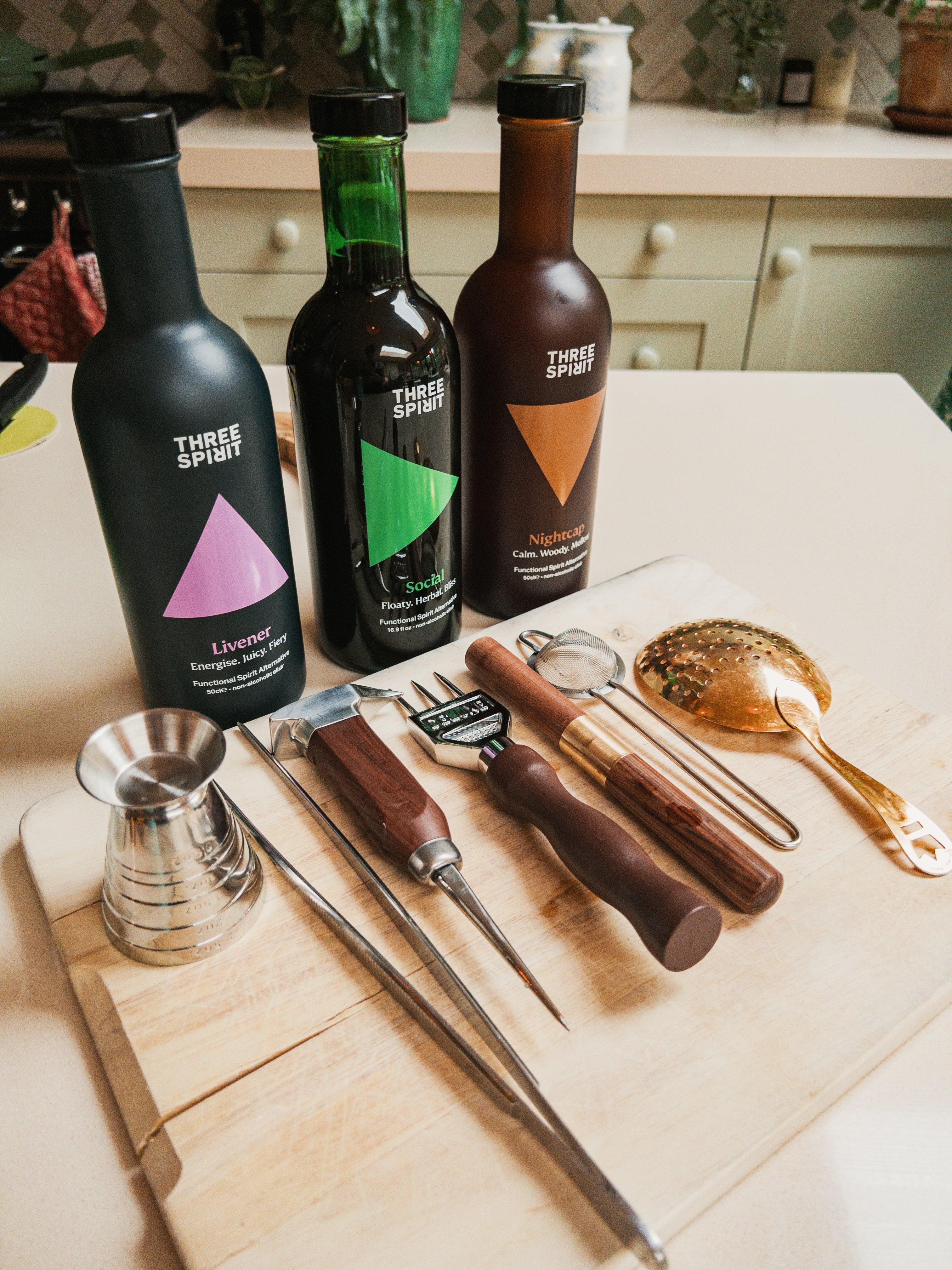Drie flessen Three Spirit alcoholvrije spirits en cocktailtools op een snijplank in keuken | World of NIX
