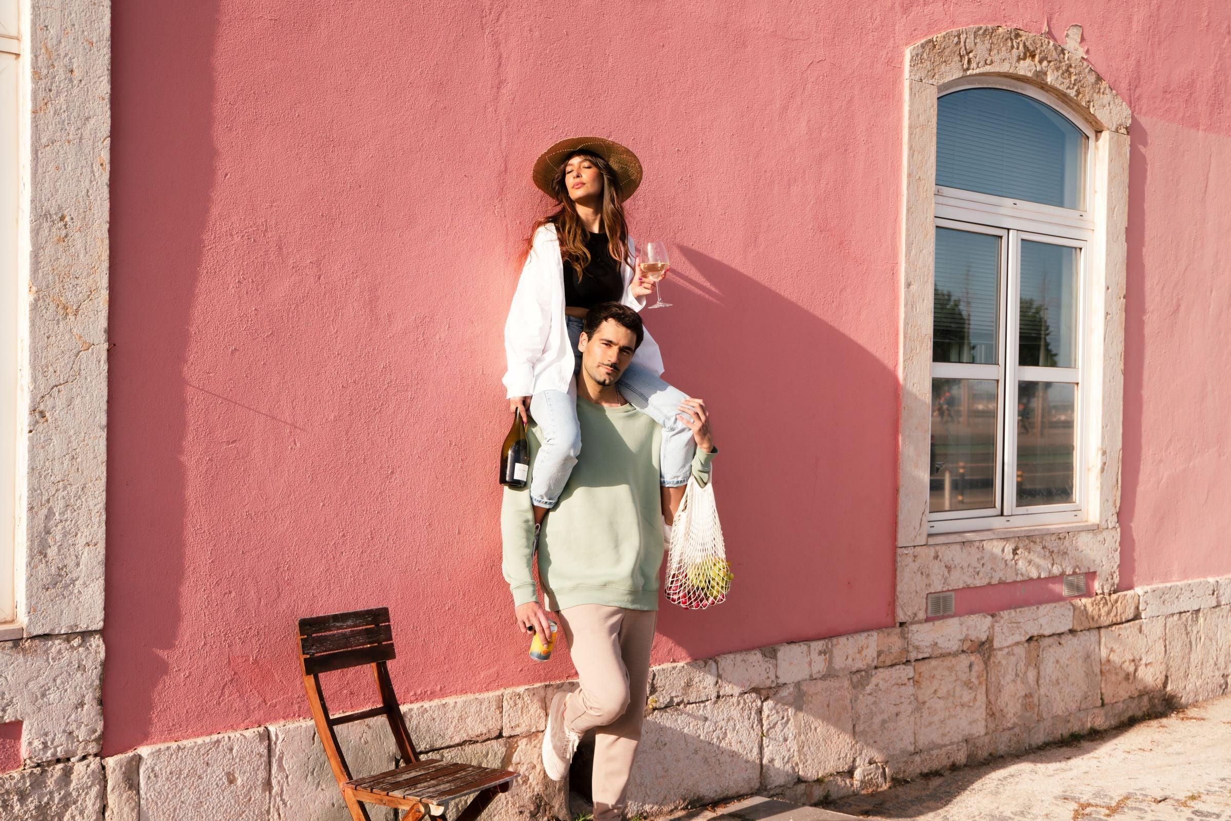 Stijlvol stel met alcoholvrije wijnflessen voor roze muur, zomerse sfeer | World of NIX