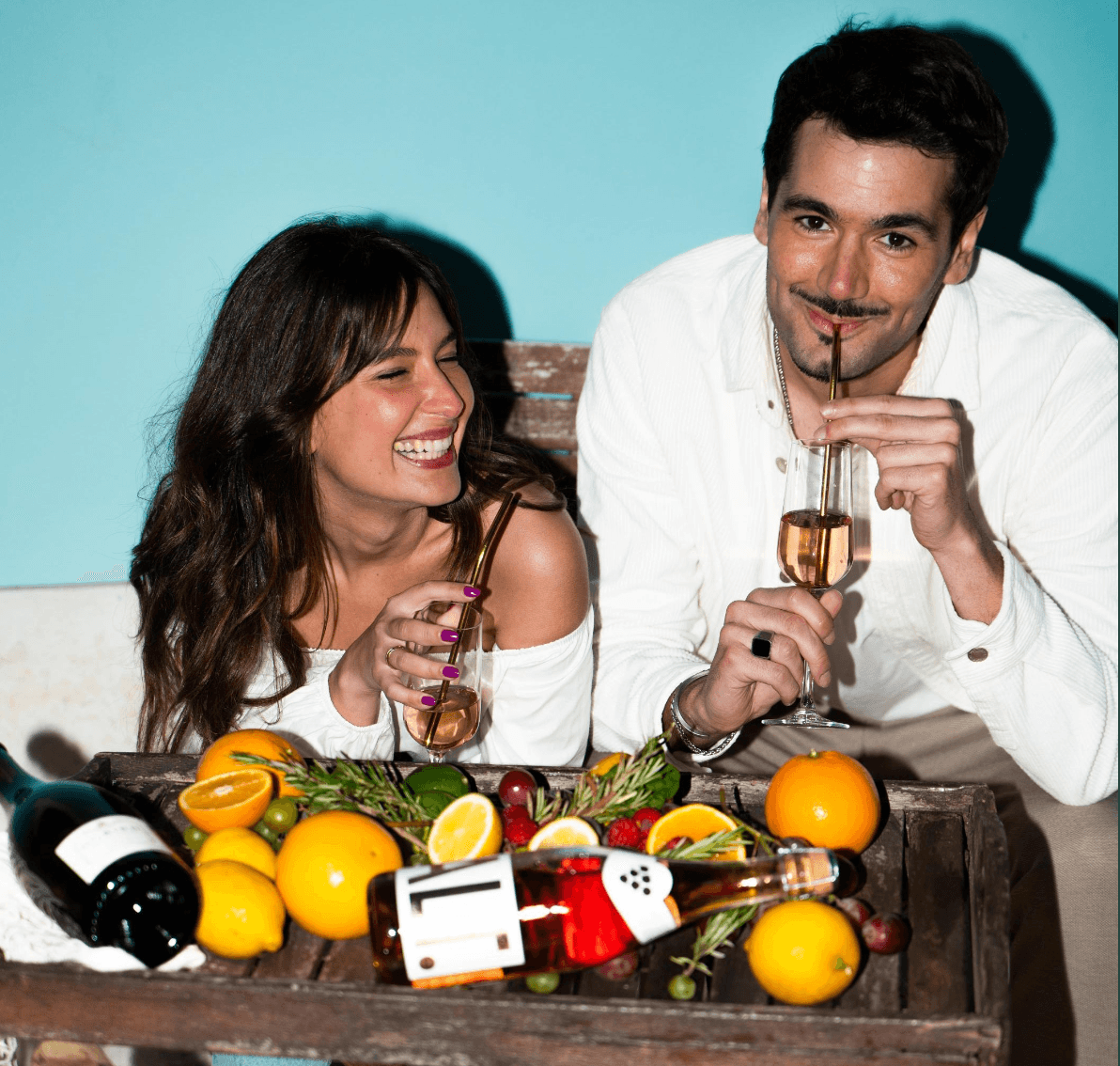 Twee lachende mensen proosten met alcoholvrije drankjes, fruit en flessen op houten tafel | World of NIX