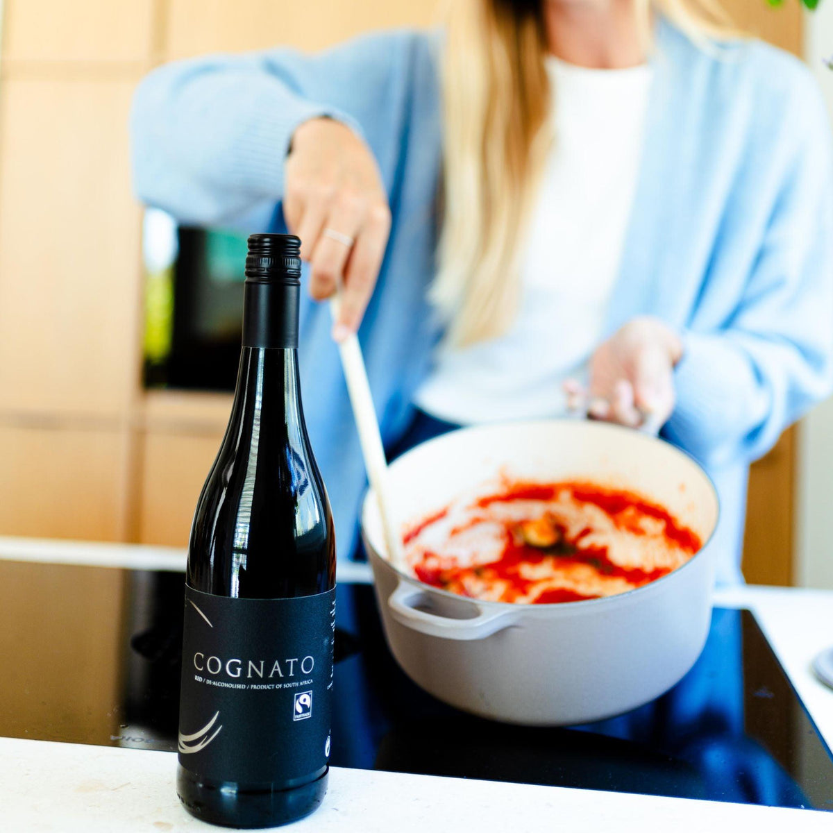 Fles Cognato alcoholvrije wijn op aanrecht, vrouw roert in pan tomatensaus | World of NIX