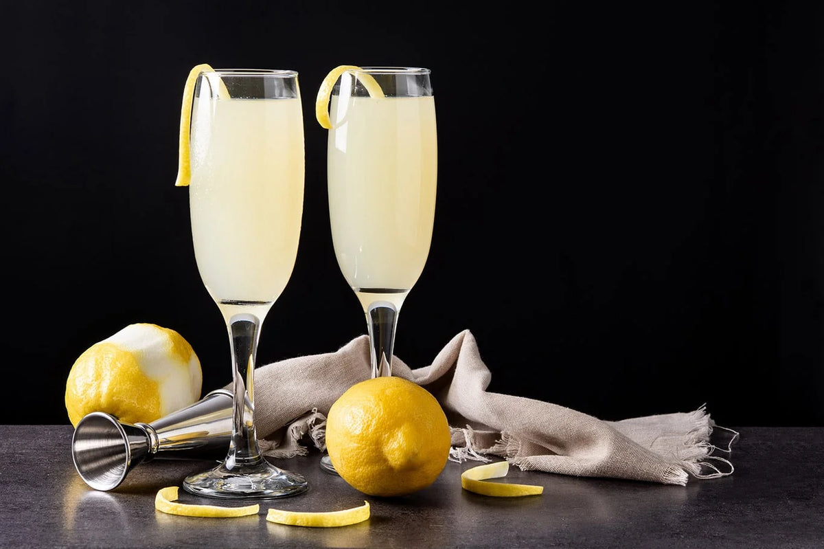 Twee French 75 alcoholvrije cocktails in flûteglazen met citroen-garnering, citroenen op tafel | World of NIX