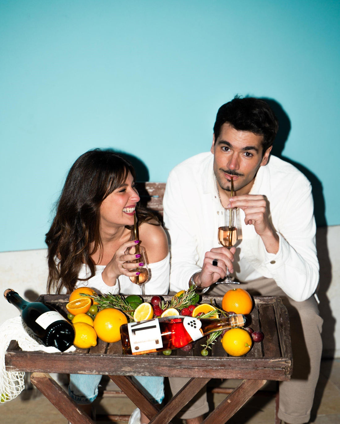 Twee mensen genieten van alcoholvrije rosé wijn met fruit op tafel tegen blauwe achtergrond | World of NIX