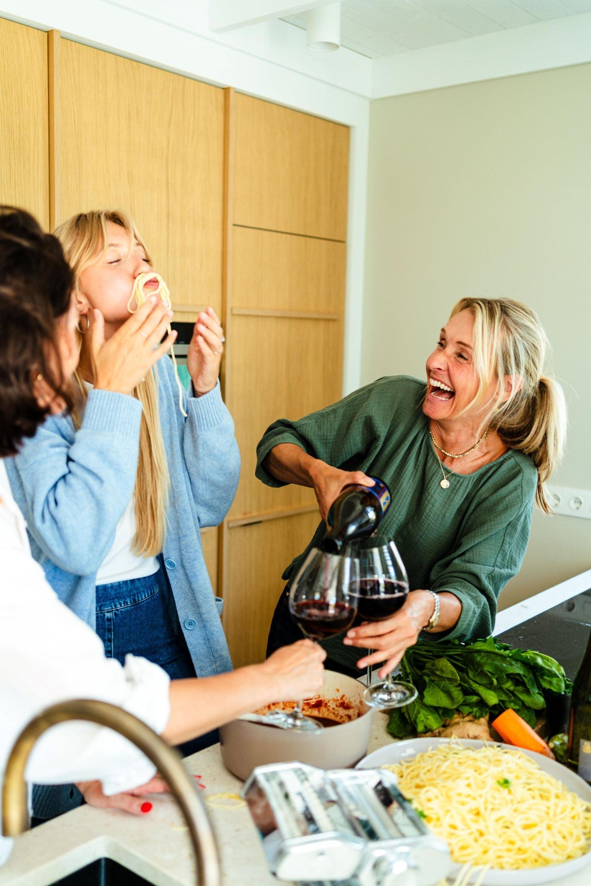 Drie vrouwen lachen samen in de keuken, maken pasta en schenken alcoholvrije wijn in | World of NIX