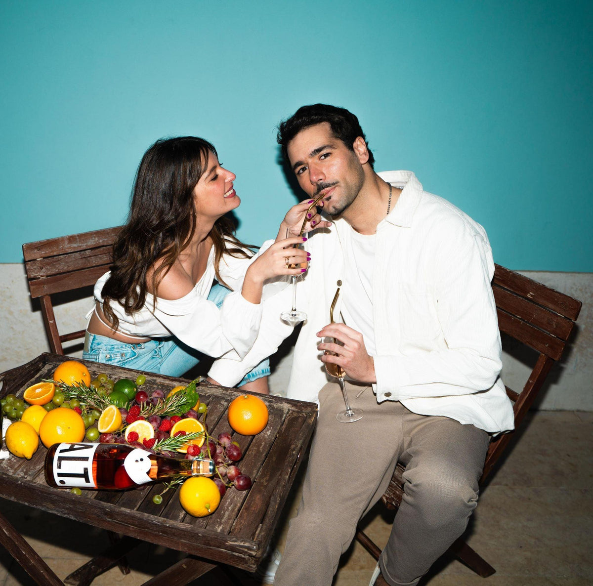 Twee mensen proosten met alcoholvrije rosé, omringd door fruit op een houten tafel | World of NIX