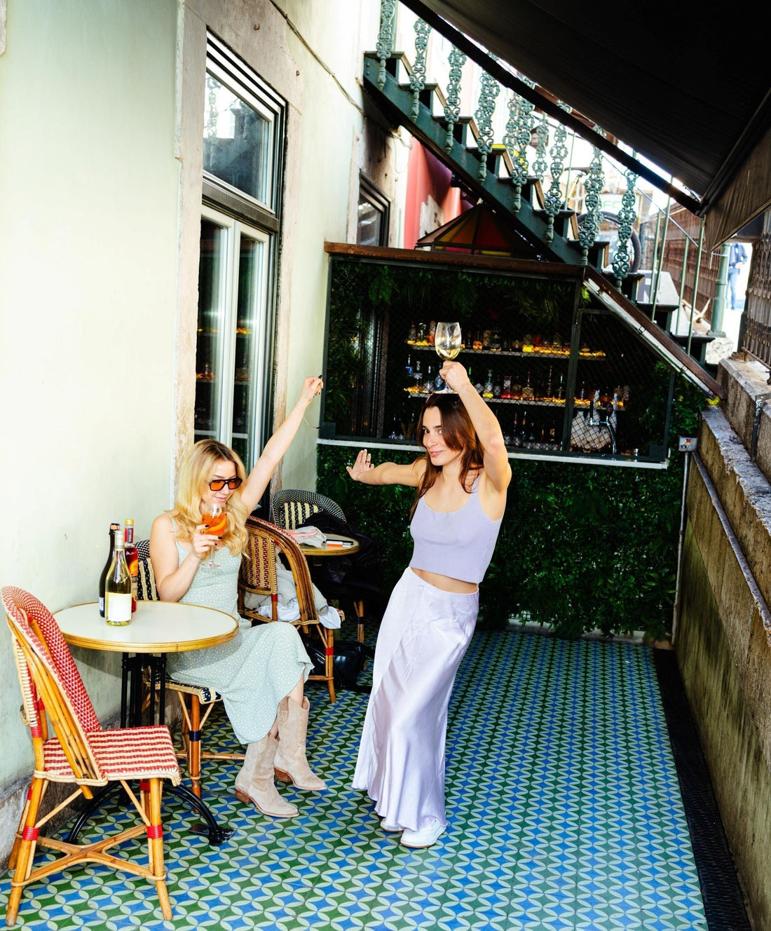 Twee vrouwen genieten van alcoholvrije drankjes op een zonnig terras met flessen wijn | World of NIX