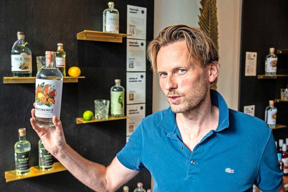 Man in blauwe polo toont fles alcoholvrije spirit, flessen op achtergrond | World of NIX