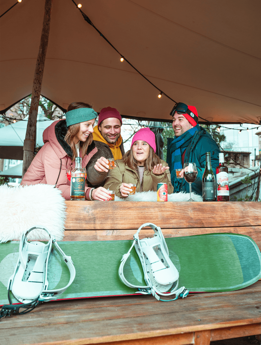 Vier mensen met winterkleding proosten met alcoholvrije dranken en snowboarden buiten | World of NIX