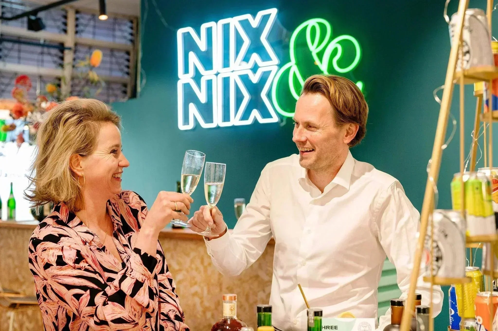 Twee mensen proosten met alcoholvrije bubbels in moderne winkel, NIX & NIX neonbord op achtergrond | World of NIX