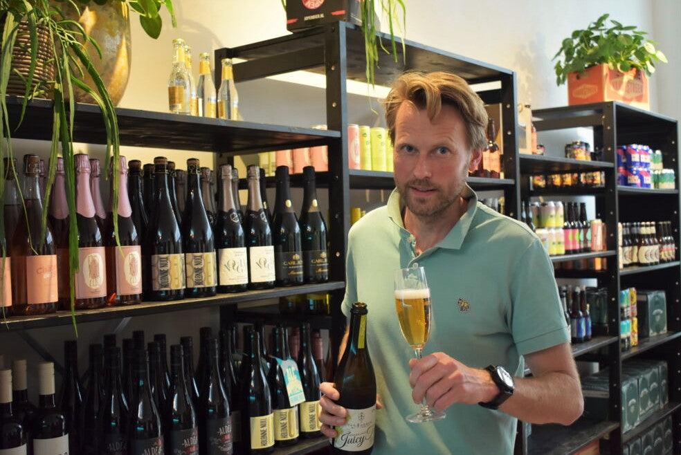 Man met glas alcoholvrij bier voor schappen met alcoholvrije dranken in winkel | World of NIX