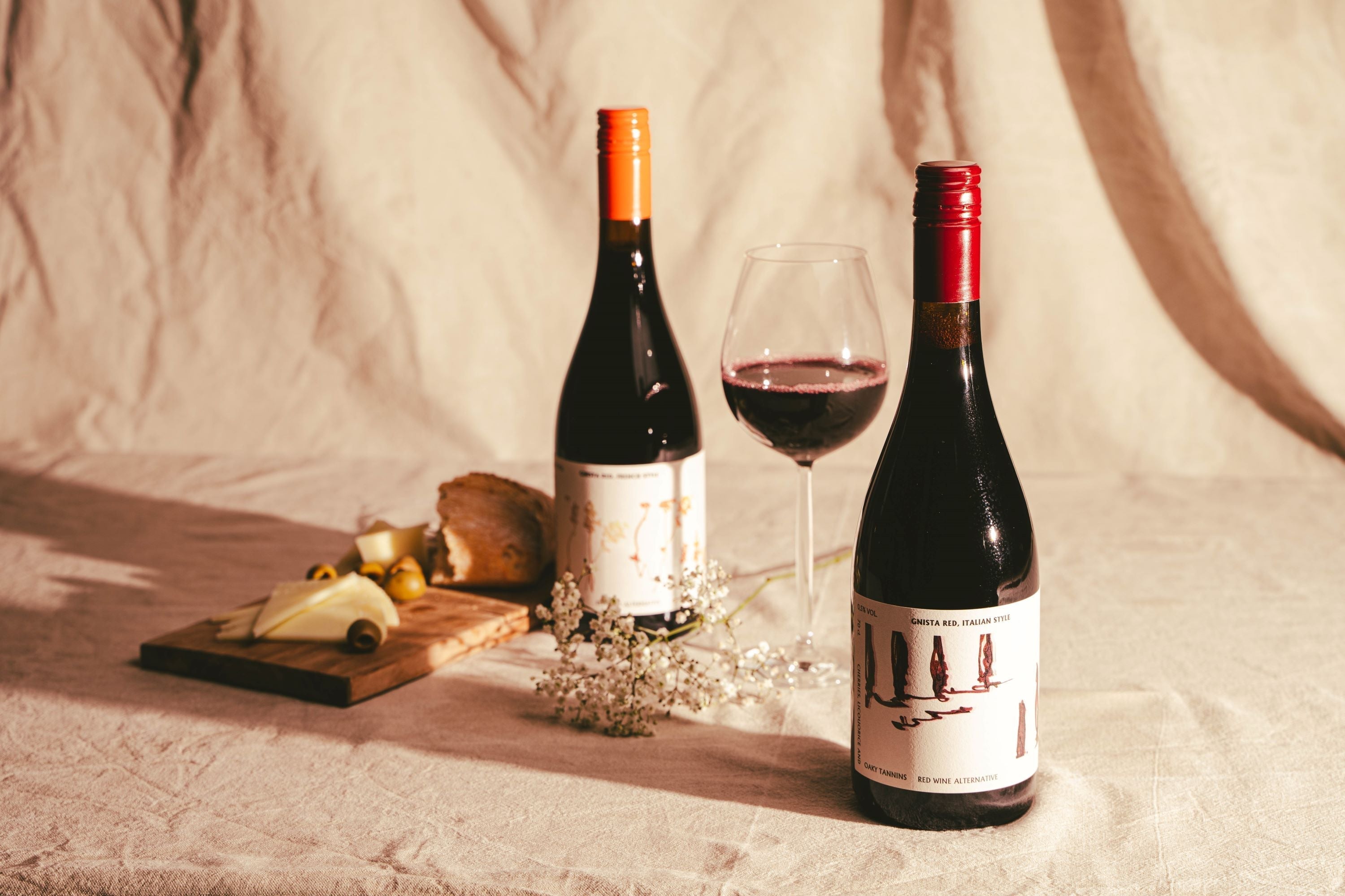 Twee flessen alcoholvrije rode wijn met kaasplankje en wijnglas op tafel | World of NIX