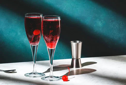 Twee Kir Royal cocktails met kersen op een witte tafel, cocktailmaatbeker ernaast | World of NIX