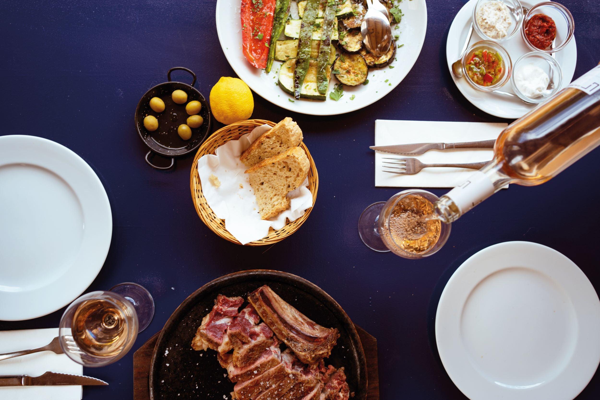 Luxe tafel met gegrild vlees, brood, gegrilde groenten, olijven en een glas sprankelende drank | World of NIX