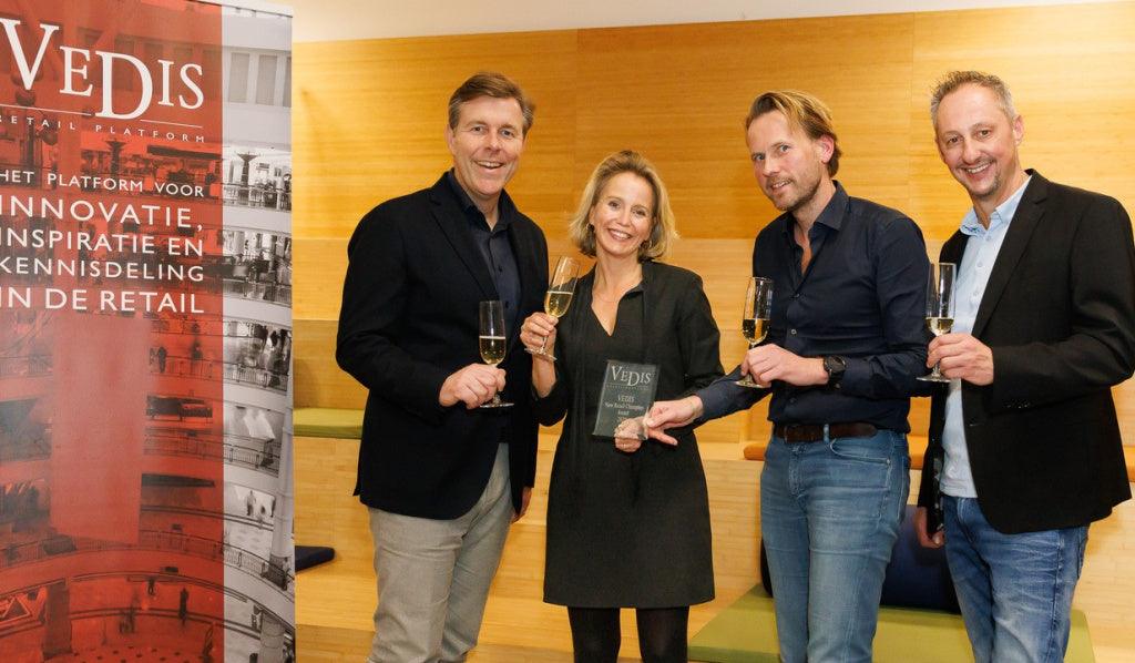 Vier mensen proosten met glazen drank en houden een VEDIS award vast, binnenruimte, retail event | World of NIX