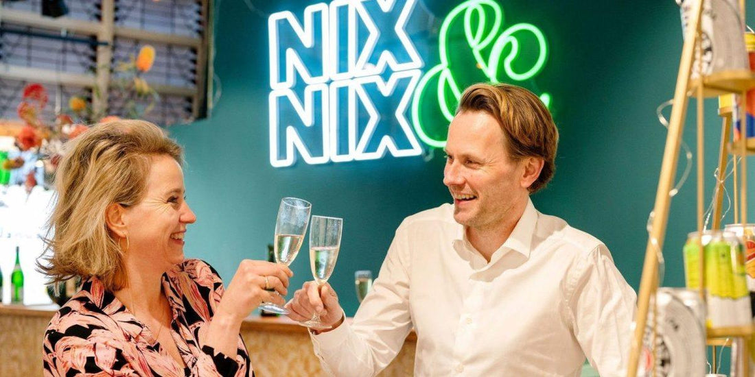 Twee mensen toasten met alcoholvrije bubbels voor NIX & NIX neonbord in winkel | World of NIX