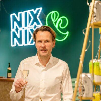 Man met glas alcoholvrije wijn in moderne winkel met neon NIX & NIX logo | World of NIX