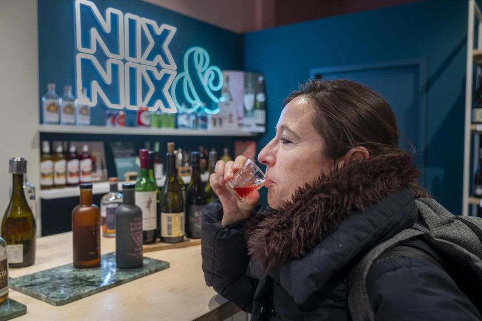 Vrouw proeft alcoholvrije drank in winkel met World of NIX neon sign en flessen | World of NIX