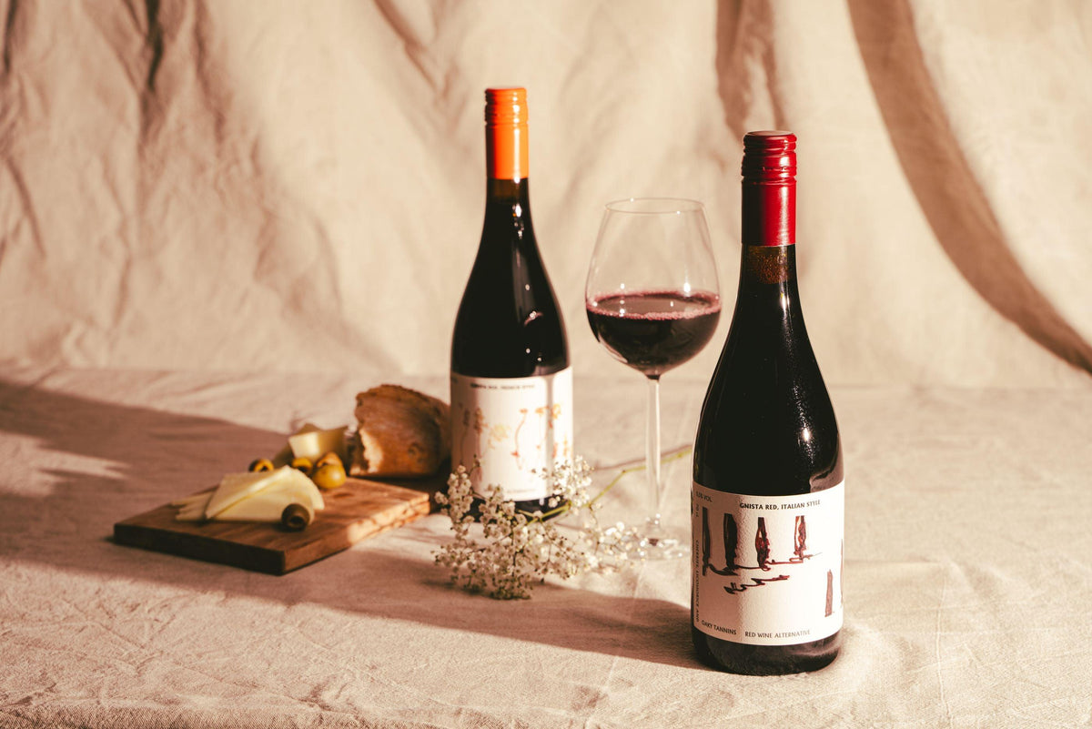 Twee flessen Gnista alcoholvrije rode wijn met kaasplankje en glas wijn op tafel | World of NIX