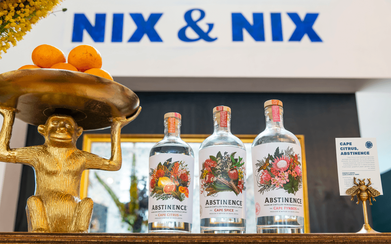 Gouden apenbeeld met schaal sinaasappels naast drie flessen alcoholvrije Abstinence spirits in winkel | World of NIX