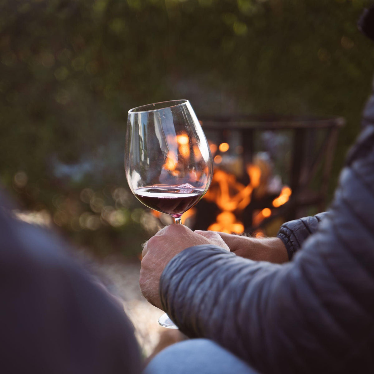 Hand met wijnglas rode wijn buiten bij vuurkorf, alcoholvrije wijn sfeer | World of NIX