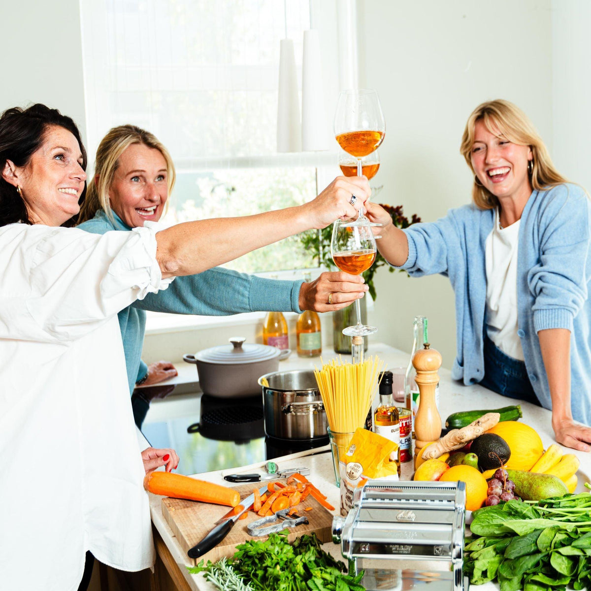 Drie vrouwen proosten met alcoholvrije drankjes in een lichte keuken vol verse groenten en pasta | World of NIX