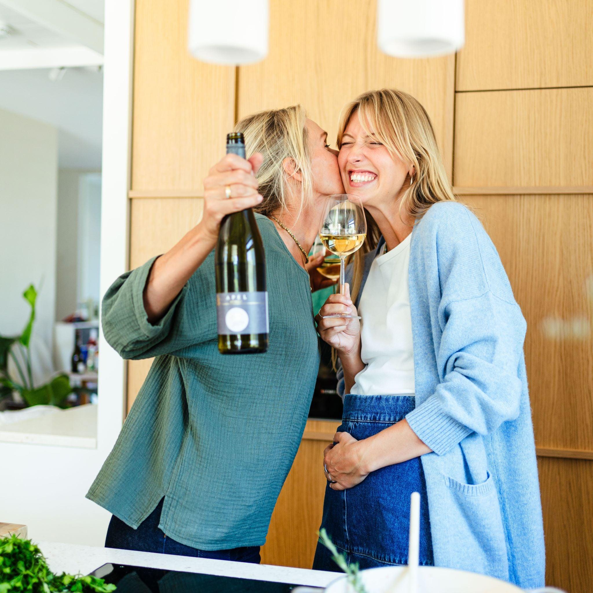 Twee lachende vrouwen in keuken met alcoholvrije wijn en wijnglas | World of NIX
