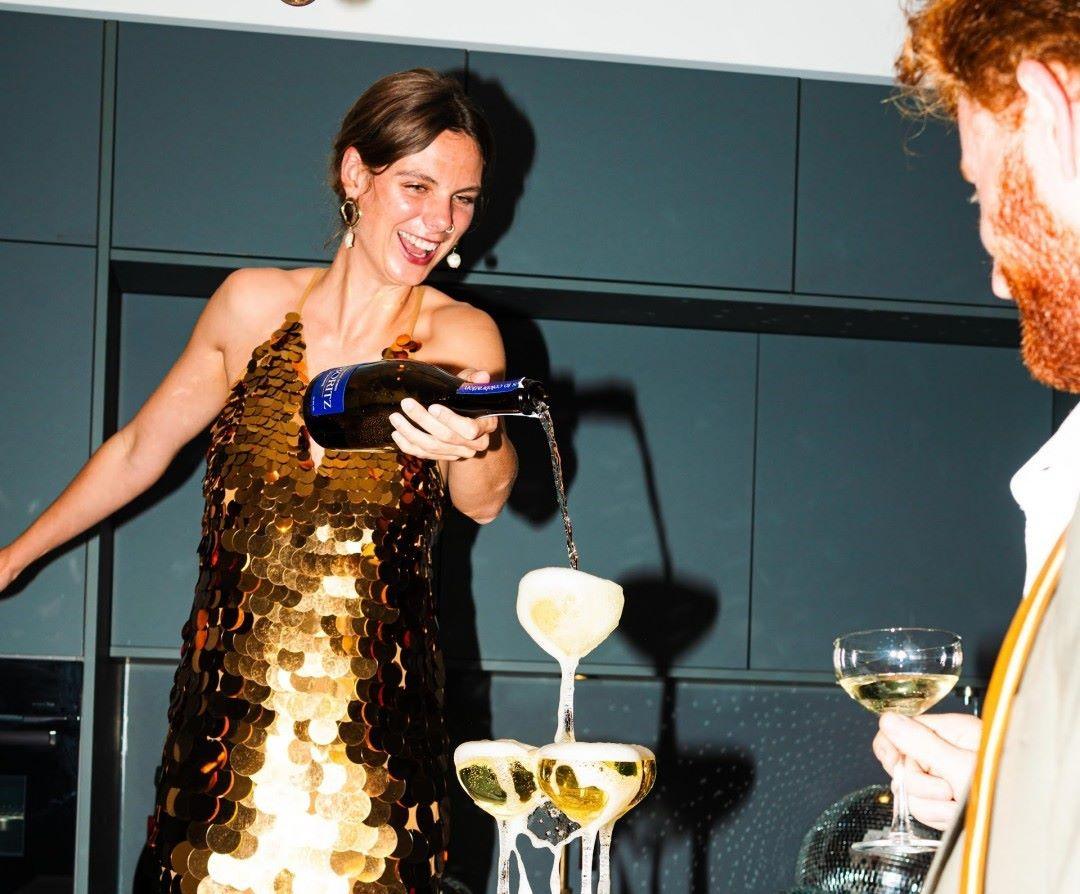 Vrouw in gouden jurk schenkt alcoholvrije bubbels in champagneglazen bij feest | World of NIX