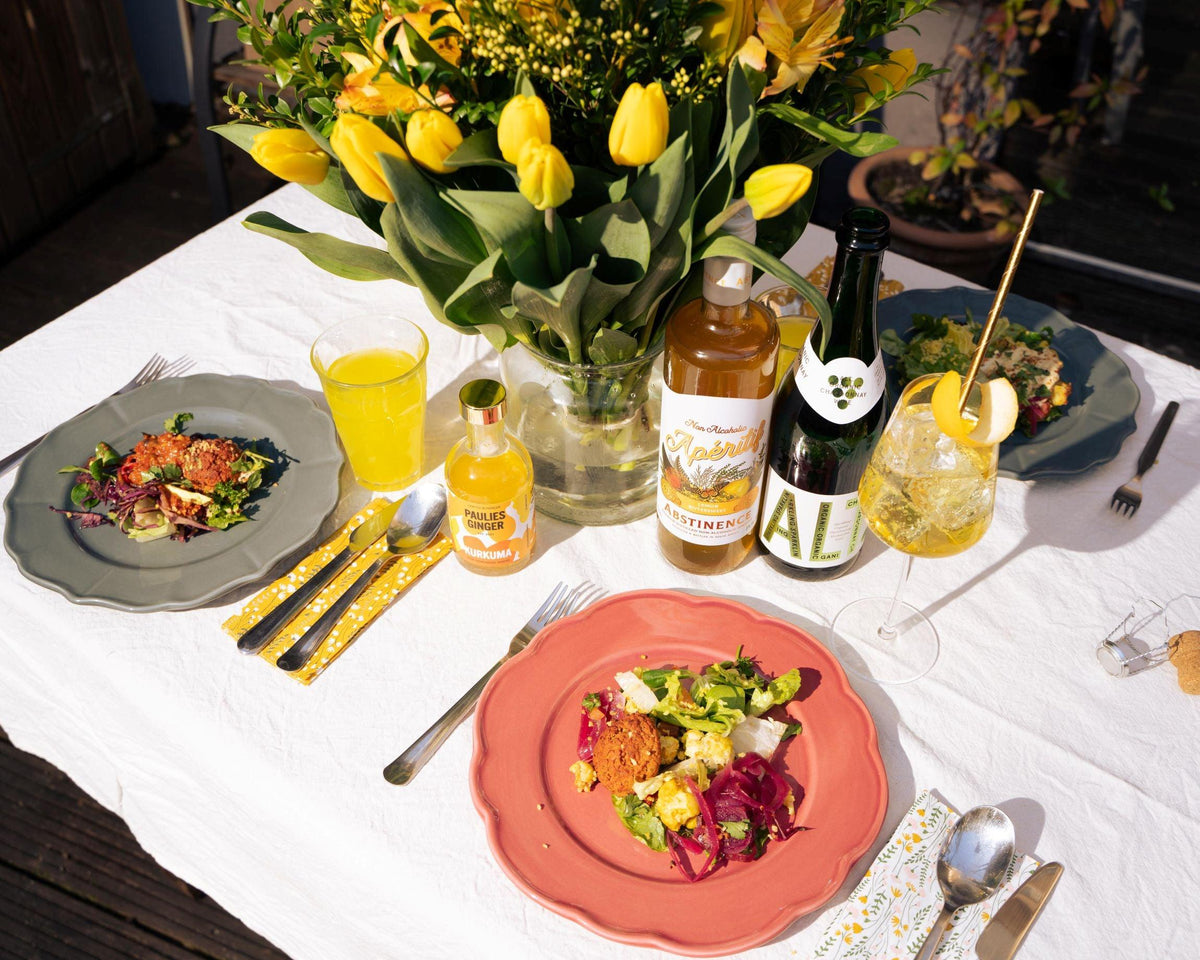 Lente tafel met alcoholvrije dranken, verse salade en gele tulpen op wit tafelkleed | World of NIX