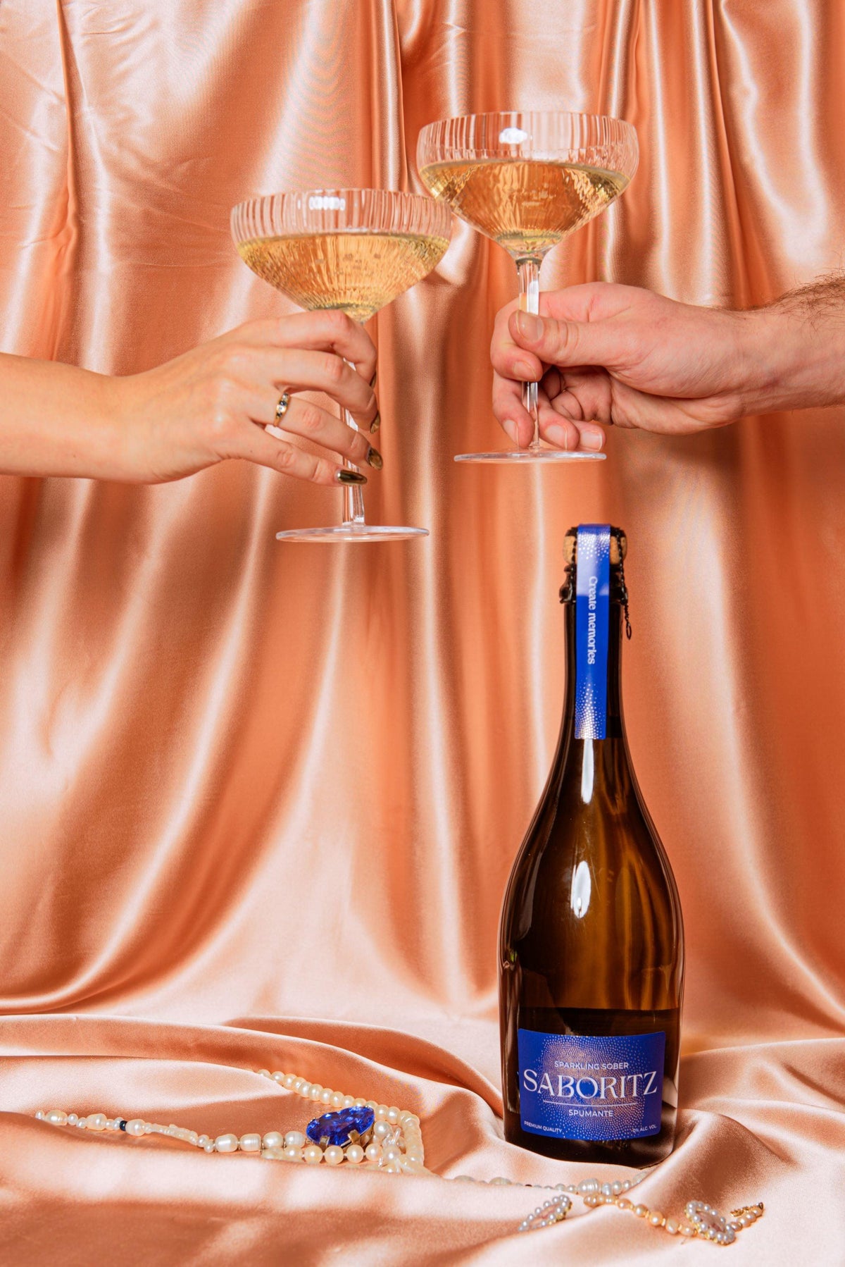 Twee handen proosten met glazen alcoholvrije bubbelwijn SABORITZ op satijnen achtergrond | World of NIX
