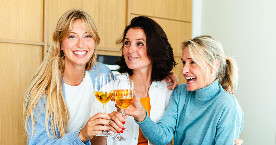Drie lachende vrouwen proosten met alcoholvrije wijn in moderne keuken | World of NIX