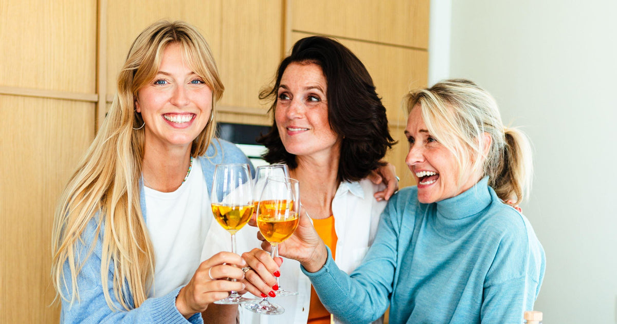 Drie lachende vrouwen proosten met alcoholvrije wijn in moderne keuken | World of NIX