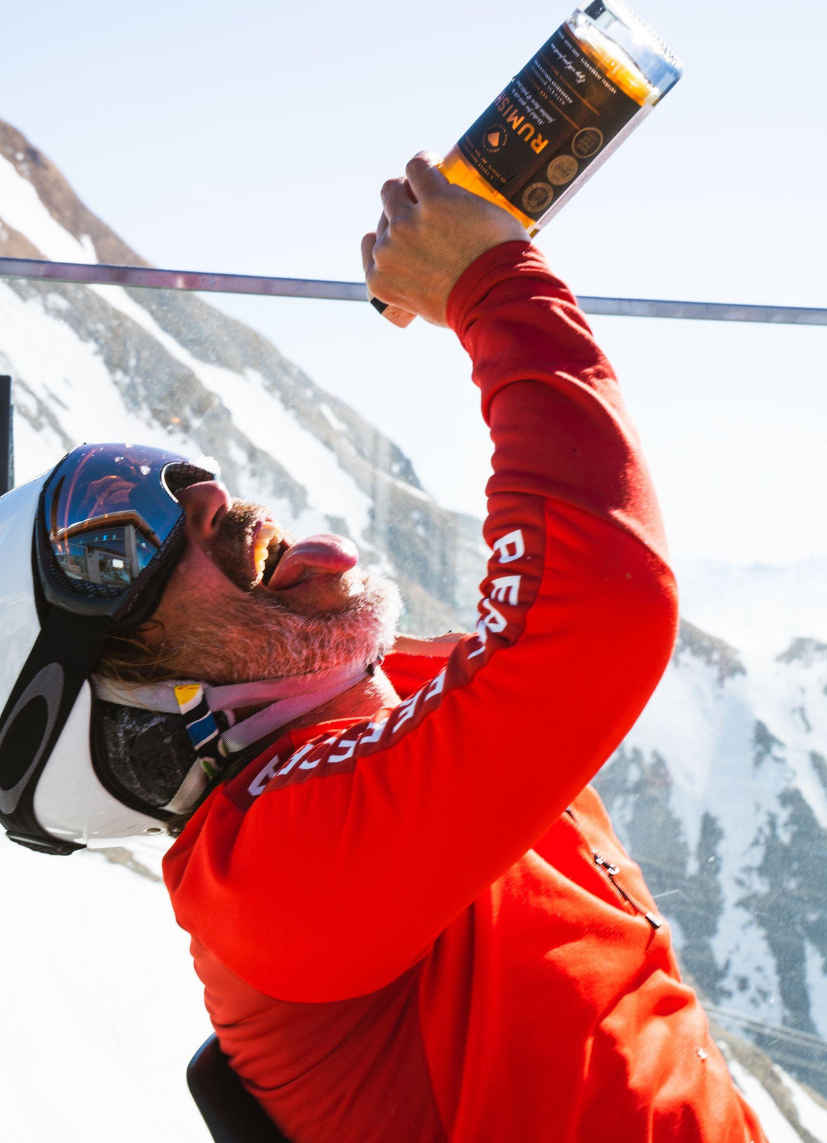 Man in rode ski-jas en helm houdt alcoholvrije drankfles omhoog in de sneeuw | World of NIX