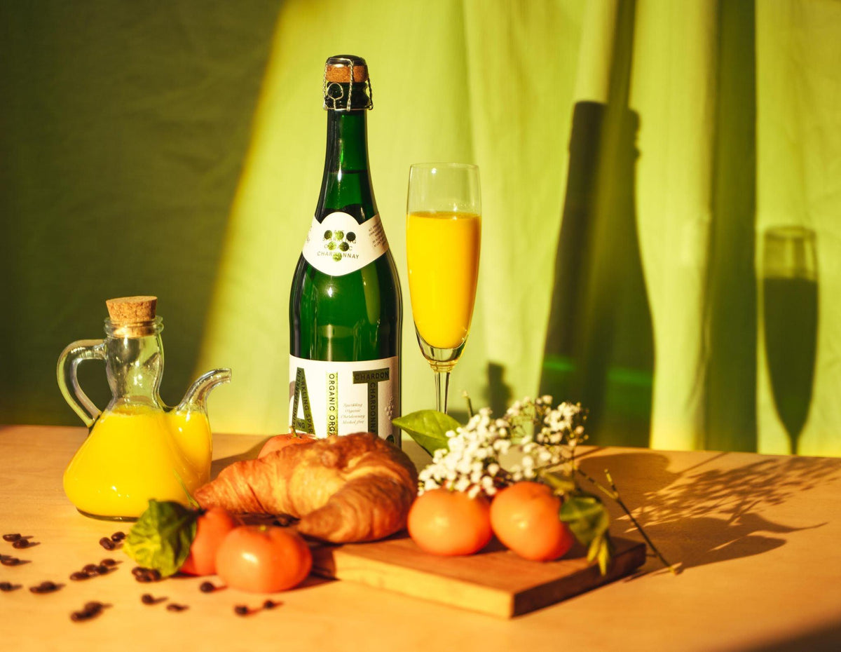 Alcoholvrije mousserende wijn met croissant, sinaasappelsap, fruit en bloemen op ontbijttafel | World of NIX