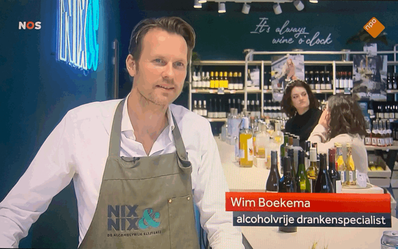 Winkelmedewerker met NIX&NIX schort tussen alcoholvrije dranken in moderne slijterij | World of NIX