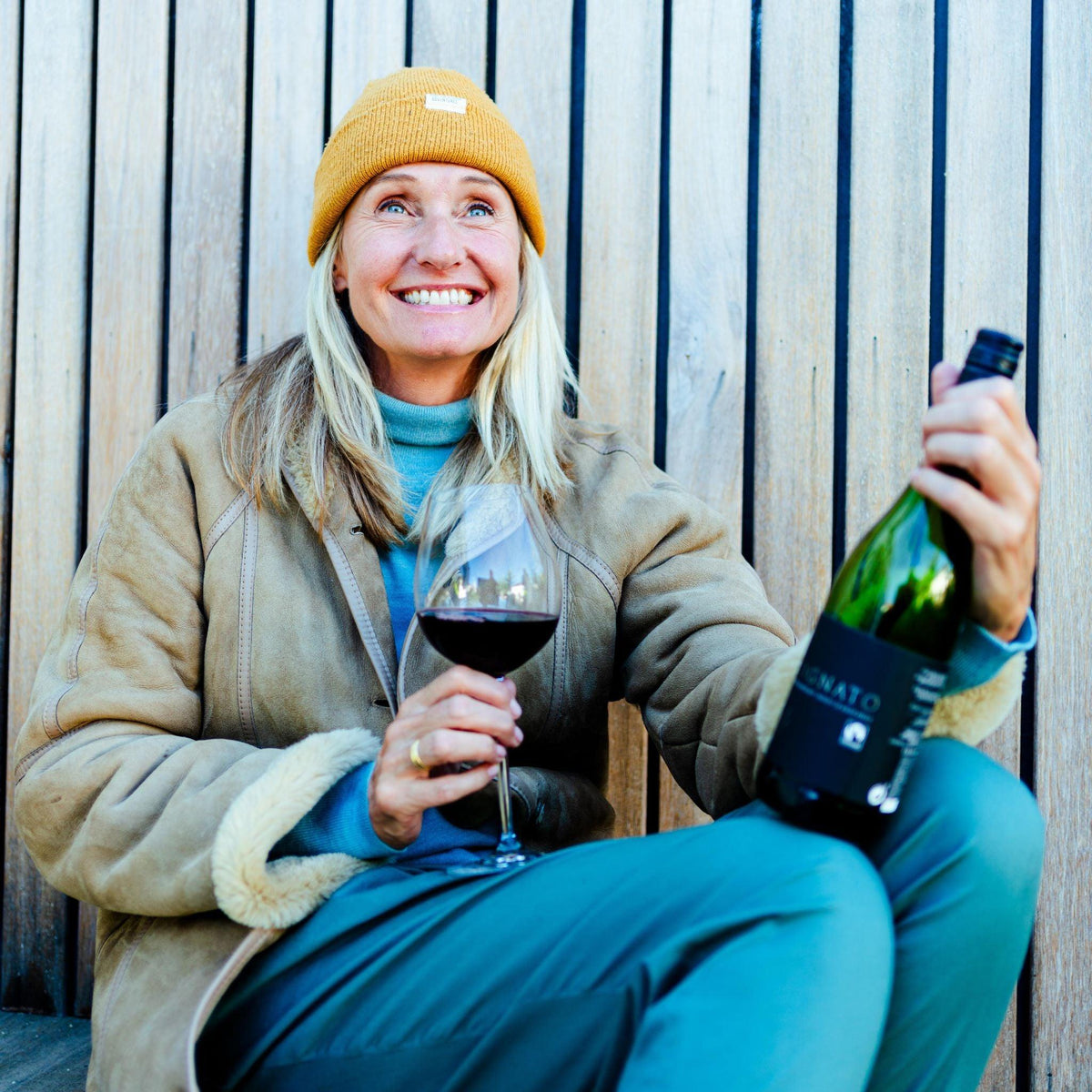 Vrouw met gele muts geniet van een glas rode alcoholvrije wijn buiten | World of NIX